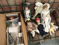 Dolls displayed on a plaid couch including porcelain and vintage dolls with some accessories and a cat figurine.