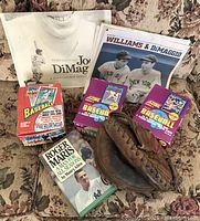 Photo showing unopened vintage Topps 40th anniversary baseball card box, two unopened 1991 Score Series 2 baseball card packs, Joe DiMaggio memorabilia book, Roger Maris biography book, and a vintage leather baseball glove.