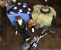 Photo showing the folded vintage 48 star American flag, Boy Scout uniform shirt, brown leather baseball mitt, two metal detectors, mannequin doll dressed in black, green pouch, and a miniature soldier trophy with American flag.