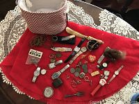Wide shot showing all items arranged on a red fabric including watches, knives, coins, jewelry, and various small items.