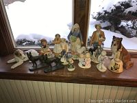 Wide view of all the figurines arranged on a window ledge showing the entire lot including porcelain and brass dogs