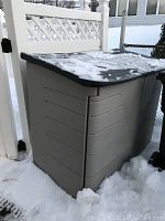 Large Rubbermaid outdoor storage container with black lid and gray body covered in some snow.
