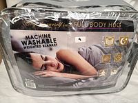 Photo of packaged weighted blanket with product branding and front label showing machine washable, full body hug theme