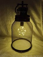 Lit LED lantern inside metal mesh cage, showing LED bulb configuration and light glow