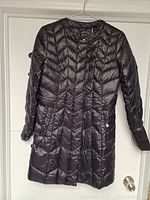 Front view of black puffer moto jacket by Via Spiga hanging on hanger showing asymmetrical zip and snap button pockets.