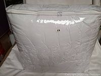 Clear plastic zippered storage bag containing white quilted comforter showing pleated knit and loop texture patterning.