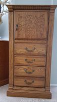 Front view of solid oak lingerie cabinet showing carved leaf design on door, lock and four drawers with metal handles.