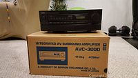 Black Denon AVC-3000 surround amplifier on original box with product details visible.
