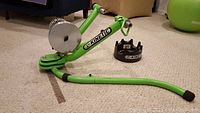 Green Kinetic indoor bicycle trainer with resistance unit and separate black front wheel riser displayed on carpet.