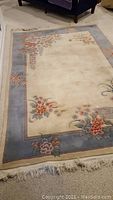 6' x 9' wool area rug with cream center and floral border in grayish-blue, showing fringed edges.