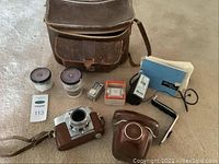 Vintage Agfaflex camera, lenses, flash, film canisters, light meter, and leather case, laid out on carpeted floor.