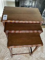 Set of three wooden nesting tables stacked together showing scalloped edges and surfaces.