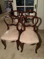 Four vintage wooden dining chairs with upholstered fabric seats arranged in room, showing front and back details