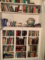 Wide view showing shelves with multiple books and a globe on top of a white cabinet with glass doors.