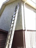 Aluminum extension ladder leaned against house wall, showing full length and structure.
