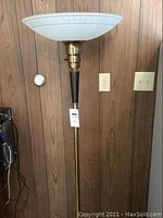 Full view of the vintage torchiere floor lamp showing its height and design against a wooden paneled wall.