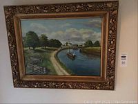Framed oil painting showing entire artwork and frame with village river scene.