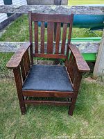 Front view of mission oak armchair showing vertical slat back, original finish, and new black leather seat.