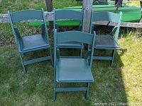 Four green folding chairs with padded seats arranged outside on grass. Showing overall condition, stackability, and seat padding.