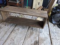 Front and side angle view of the wooden shelving unit showing rectangular shape and hairpin legs placed on wooden floor.