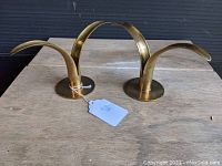 Pair of vintage brass candlestick holders on wood surface showing their height and curved petal design.
