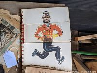 Close-up of the red spiral-bound book with colorful illustrated papers depicting a running cartoon character.