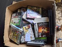 Top view of a large box filled with assorted empty video game cases mostly Nintendo DS and Game Boy Advance. Visible titles include Harry Potter and a football game.