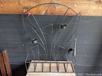 Front view of the wrought iron wall mounted candle holder showing the three circular candle cups, decorative curved iron bars, and wooden plank base.