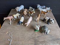 Overview of all animal figurines arranged on wooden surface including tiger, zebra, panda, giraffe, lion, horse, cow, tortoise, goose, pigs