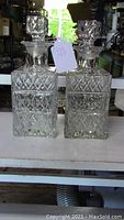 Image of a pair of matching etched glass liquor decanters on a table with tags attached.