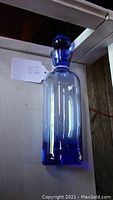Cobalt blue glass liquor decanter with rounded stopper, clear upper body, cobalt blue base and neck, displayed upright on white surface.