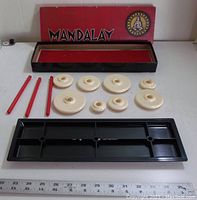 Game box with lid removed showing playing pieces, red sticks, and black plastic board inside.