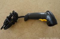 Side view of the barcode scanner showing black plastic body and yellow trigger.