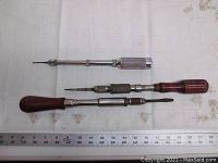Three antique Yankee screwdrivers laid flat with ruler for scale on cloth background showing condition and structure