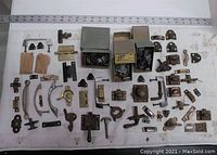 Top-down view showing assorted metal hinges, door handles, latches, and mounting hardware arranged on a white sheet with a ruler for scale.