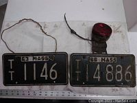Two antique Massachusetts license plates with a red tail light on one plate, showing the full lot contents and condition.