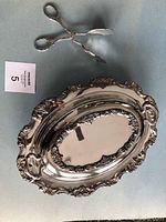 Photo showing oval silver serving dish and matching serving tongs with floral chasing and detailed carving.