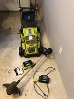 Full view of lawn mower, trimmer, battery and charger on concrete floor