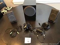 Full view of small speaker set with two satellite speakers, subwoofer, connected cables and power adapter on table.