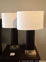 Two bedside lamps side by side showing the brushed nickel bases and mahogany colored bodies with cream drum shades
