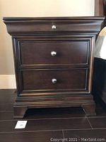 Solid wood bedside table with three drawers, mahogany finish, metal knobs, close-up showing drawer fronts