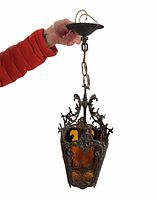 Full view of the antique hanging light fixture held by a person in a red jacket showing chain suspension and ornate metal frame with amber colored glass panels.