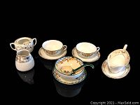 View of the set including two matching Nippon cups and saucers, creamer, sugar bowl, Noritake bowl with spoon and plate, and Nippon gravy boat with underplate on black background.