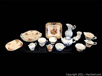 Full view of the assortment showing plates, creamers, tea cups, a miniature vase and a Delft style tea pot arranged on a black surface.