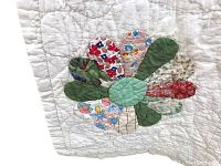 Close-up of one flower block showing multi-patterned fabric petals in red, green, blue and beige tones with central green circle applique on white quilt background