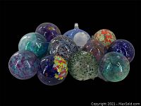 All twelve hand blown glass friendship balls and a hummingbird feeder displayed with varied colors and sizes on black background.