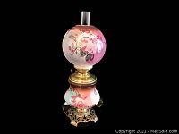 Front angled view of the double globe oil lamp showing floral painted glass globes atop ornate brass base and mid section. Electrical cord visible.