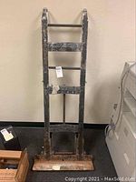 Front view of worn refrigerator dolly with black paint chipping and rust spots, standing upright against a beige wall