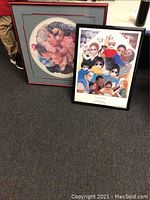 Two framed children portrait posters leaning against a wall on the carpet. Left is a Margaret Keane poster with muted colors, right is a larger poster with diverse children and adults framed in black.