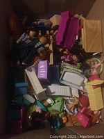 Box filled with assorted small dollhouse furniture pieces and dolls.